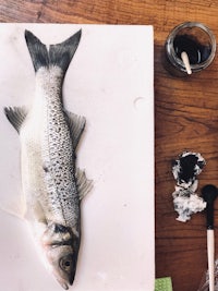 a fish is sitting on a table next to a bottle of paint