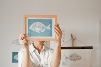 a woman holding up a framed print of a fish