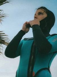a woman in a blue wetsuit standing next to palm trees